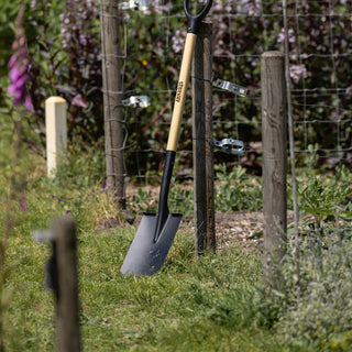 Houten steelgereedschap opgesteld langs tuinhek