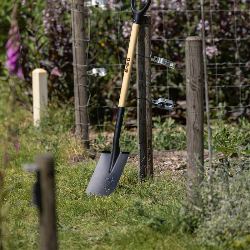 Houten steelgereedschap opgesteld langs tuinhek